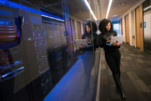 A woman using a laptop near servers.